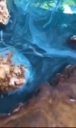 Detaj i afërt i epoksit blu-smerald që rrjedh mes copave të drurit